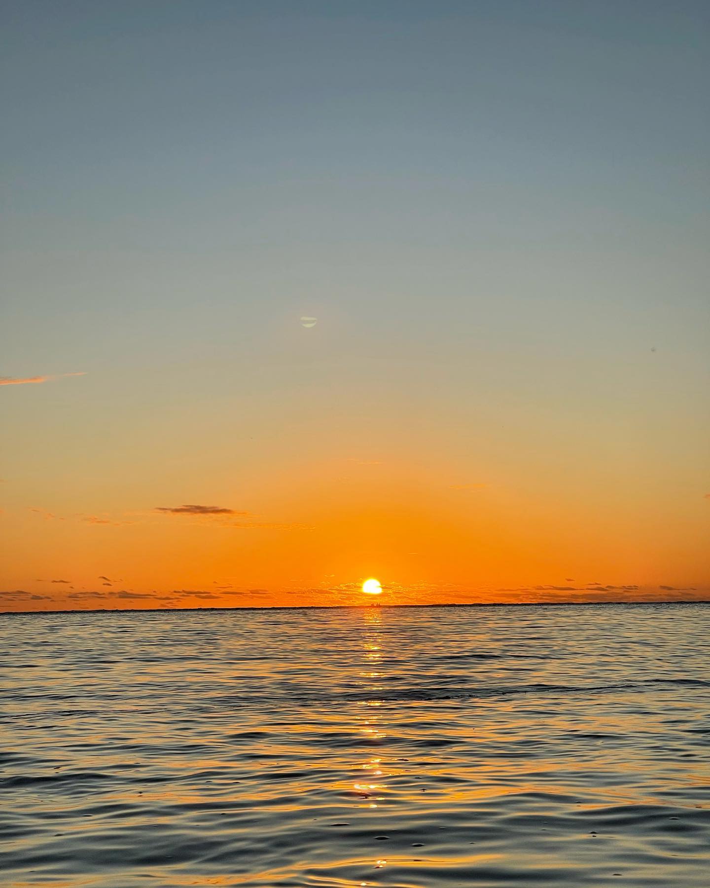 The sun setting over calm Pacific water with a long reflection toward shore