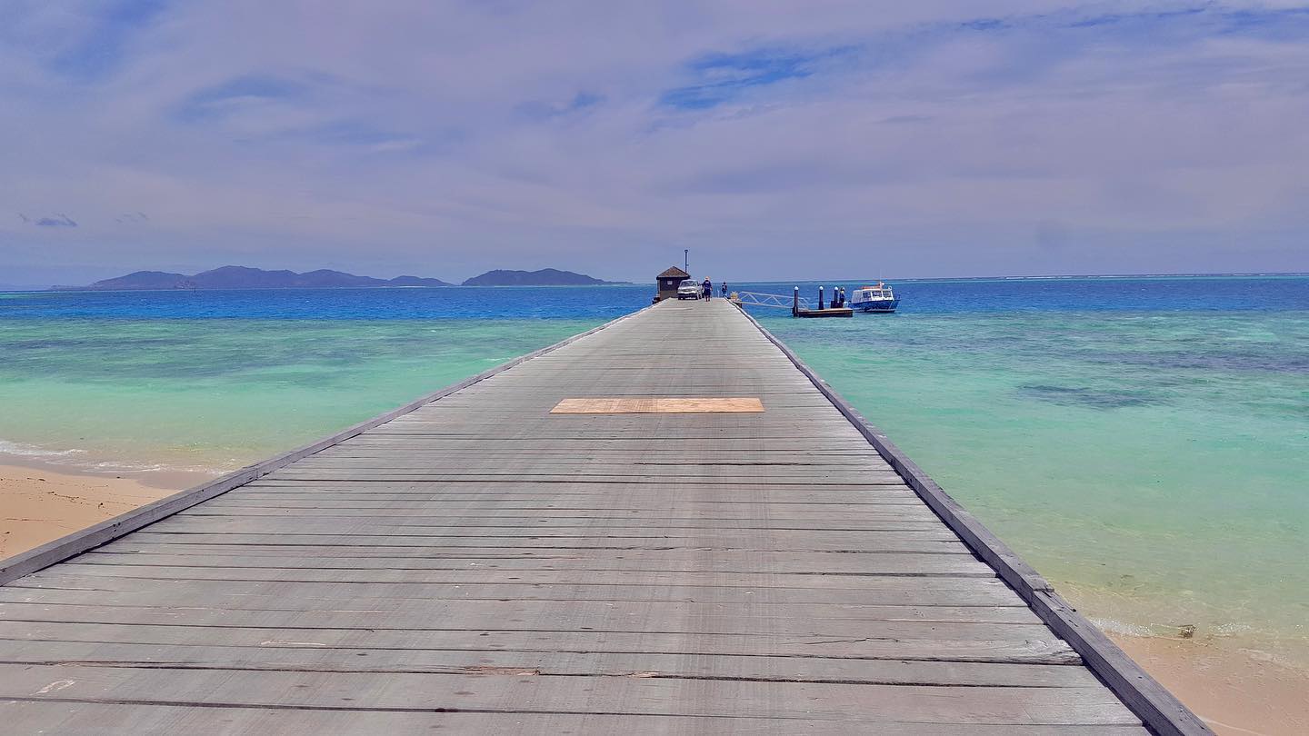 A long wooden jetty creating a pathway across turquoise Pacific water